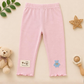 Pink baby leggings with a label and bear design on a beige background with toys and leaves.