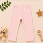 Pink baby pants on a beige background with toys and leaves.